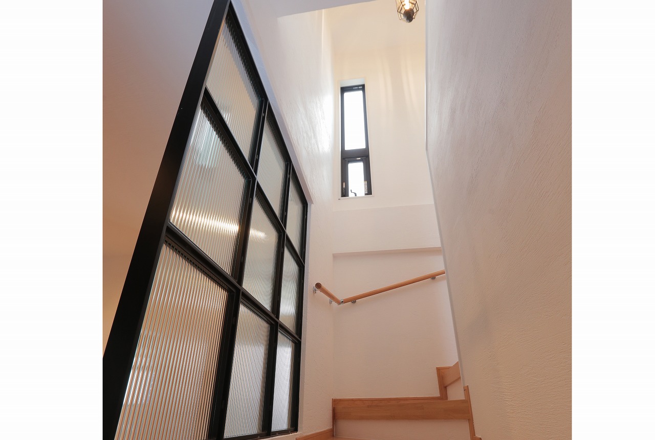 アイアンのガラスパーテーションで仕切られた階段を昇ると、お施主様セレクトのペンダントランプの柔らかい光が。階段室の漆喰壁にエレガントに反射します。