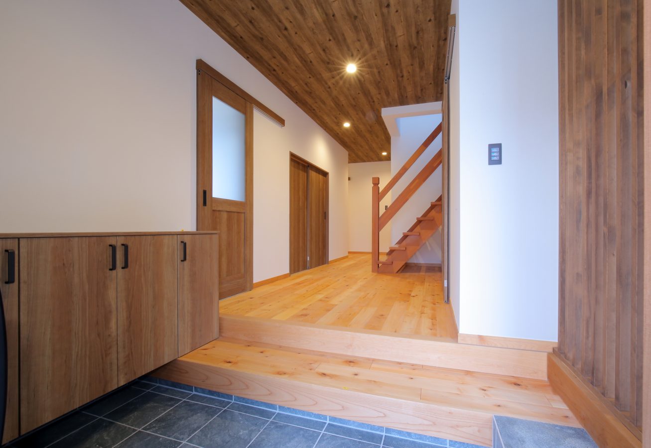木目調の天井クロスとダークグレーのタイルがいいコントラストを生んでいる玄関ホール。